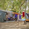 Area campeggio con camper, tavoli da picnic, amaca e canoe sotto alberi.