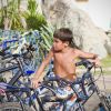 Bambino in costume da bagno vicino a biciclette parcheggiate. Sfondo con piante e rocce.