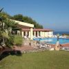 Piscina vicino a un edificio giallo, vista del mare, prati e palme.