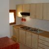 Cucina con armadi chiari, piano cottura, lavello e piccola finestra. Tavolo vicino.