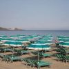 Ombrelloni verde acqua su una spiaggia sabbiosa con mare calmo sullo sfondo.