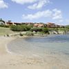 Spiaggia con mare calmo e villette sullo sfondo.