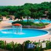 Una piscina circolare con giochi d'acqua, circondata da verde e lettini.