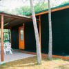 Casetta in legno scuro con veranda, tavolo e sedie bianche all'esterno, circondata da alberi.