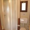 Un bagno con una doccia semicircolare e un gabinetto sotto una piccola finestra.