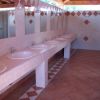 Una fila di lavandini con specchi sopra in un bagno piastrellato.