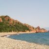 Una spiaggia di ciottoli con mare azzurro e colline verdi in lontananza.