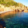 Costa rocciosa con acqua trasparente e vegetazione sullo sfondo.